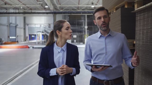 Two factory floor managers discussing work while walking and looking at tablet