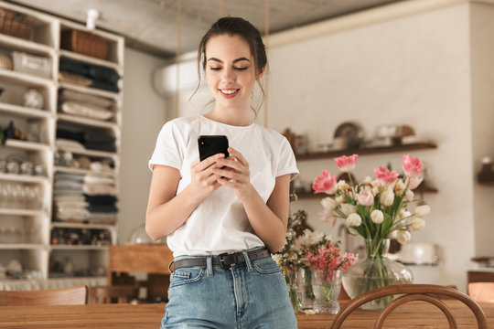 Image Of Young Nice Woman Typing On Cellphone And Smiling In Cozy Kitchen