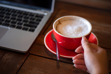 Woman's hands are lifting a cup of red coffee. With a notebook computer placed beside Placed on natural wood floor