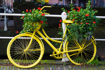 Fototapeta na wymiar yellow painted bike against with flower pots, geraniums, against white fence along canal in Netherlands