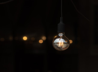 Vintage filament lamp with coil shape light hanging from the ceiling of dark background.