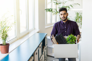 business, firing and job loss concept. Sad fired indian male office worker holding box of his...