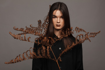 Portrait of a strict model in black clothes and with a dry fern