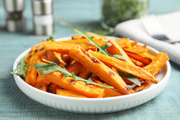 Plate with baked sweet potato slices and arugula on wooden table, closeup