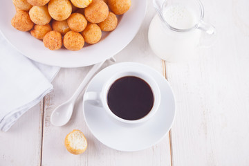 Cup of coffee with small balls of freshly baked homemade cottage cheese doughnuts in a plate on a background.