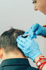 A young man with a bald spot in the office of a trichologist cosmetologist. Mesotherapy of hair and...
