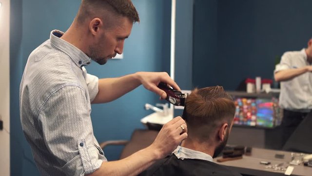 Close up shot of man getting trendy haircut at barber shop. Male hairstylist serving client, making haircut using machine and comb