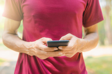 close up handsome man use hand typing mobile phones and touch screen working with app devices in park with sunrise and green blur nature background.