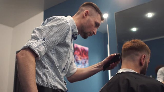 Close up shot of man getting trendy haircut at barber shop. Male hairstylist serving client, making haircut using machine and comb