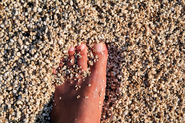Top view of man standing bare feet on beach. Texture of bottom, leg and foot of man drowning with sweeping colorful stone below on rocky stones beach in sea with waves and foam, water ripples of sea.