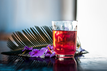 Extracted tincture or extraction of rosemary flower in a glass on wooden surface along with rosemary flowers and leaves.