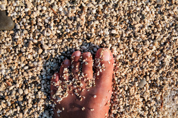 Top view of man standing bare feet on beach. Texture of bottom, leg and foot of man drowning with sweeping colorful stone below on rocky stones beach in sea with waves and foam, water ripples of sea.