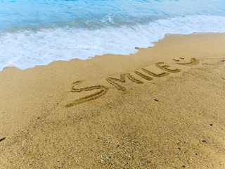 writted word smile and smiling smiley on wet sand near the sea