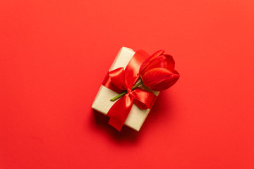 Birthday, Christmas and sale concept. Christmas gift box with red tulip flower tied with bow on a red background.