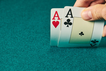 close-up of two aces held in one hand on the green game mat on the right side of the image to leave room for editing.