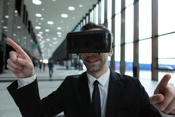 Smiling businessman in VR headset enjoying exploring visualized virtual reality world in business center lobby
