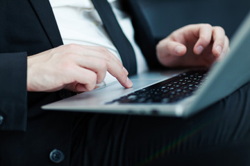 Closeup side view hands of unrecognizable businessman in formal suit and tie using touchpad on laptop computer placed on his lap