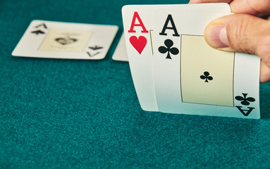 close-up of two aces held in one hand on the green game mat on the right side of the image to leave room for editing.