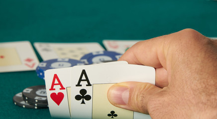 close-up of two aces held in one hand on the green game mat on the right side of the image to leave room for editing, Other cards are on the mat