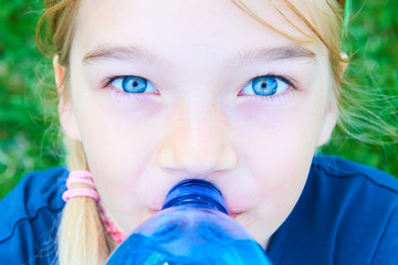 Close up portrait of adorable girl with blue eyes drinking water from plastic blue bottle with...