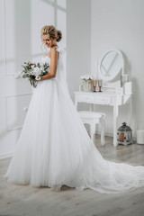 Fototapeta na wymiar Bride with a beautiful hairstyle. Model blonde in a wedding dress in white interior