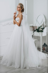 Fototapeta premium Bride with a beautiful hairstyle. Model blonde in a wedding dress in white interior
