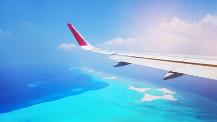 Fototapeta na wymiar View of airplane wing flying in the blue sky above Maldives island.