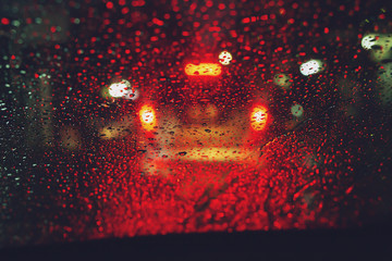 Drops Of Rain Drizzle on the glass windshield in the night. street in the heavy rain. Bokeh Tail light. soft Focus. Please drive carefully, slippery road. traffic jam car.