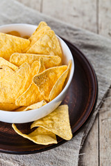 Mexican nachos chips in white bowl on brown ceramic plate closeup on linen tablecloth.