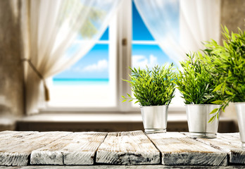 Wooden table of free space for your decoration. Small plant and summer window with sea landscape and beach. 