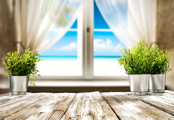 Wooden table of free space for your decoration. Small plant and summer window with sea landscape and beach. 