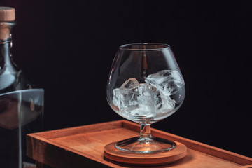 Chipped ice in a transparent brandy glass, on a wooden box on a black background.