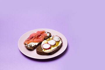 Morning breakfast of assorted sandwiches with various fillings: with fish, cheese and cucumber on a purple background.