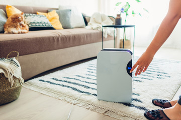 Woman turns dehumidifier on using touch panel at home. Modern airdryer device for cleaning air