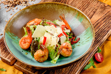 Traditional Caesar salad with shrimps, tomatoes, lettuce, eggs, parmesan and croutons in a green-brown plate on a concrete background. Beautiful composition with malt and vegetables