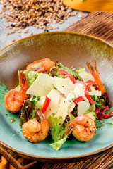Traditional Caesar salad with shrimps, tomatoes, lettuce, eggs, parmesan and croutons in a green-brown plate on a concrete background. Beautiful composition with malt and vegetables