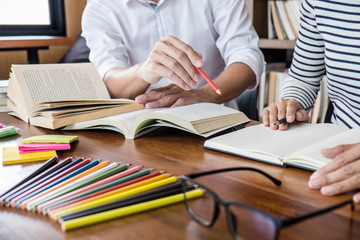 High school or college student group sitting at desk in library studying and reading, doing...