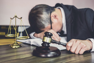 Judge gavel with lawyers, Gavel on wooden table and Counselor or Male lawyer is tired and migraine headaches during hard working on a documents at law firm. Legal law, advice and justice concept