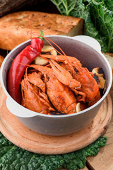 Beer Snack. Boiled crawfish in a cast-iron pan on a light wooden board on a dark wooden table. Close-up. Space