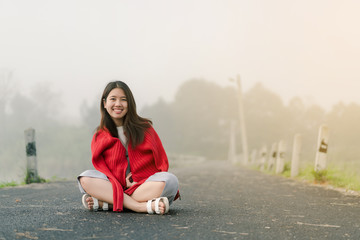 Asian teenager Wearing a red sweater Sitting in the middle of the road by the reservoir In the morning mist