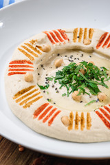 Hummus with greens in a round white plate on a wooden background. Close-up. Space. Middle Eastern cuisine. 