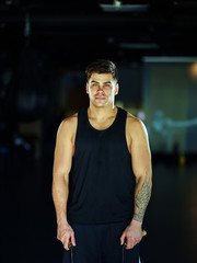 Fototapeta na wymiar Portrait of strong young boxer with tattoo on his arm looking at camera holdng jump rope in his hands and preparing for exercise