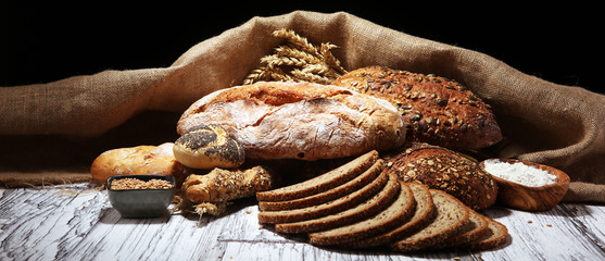 Assortment of baked bread and bread rolls on rustic white bakery table background