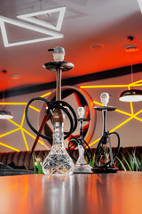 Fototapeta na wymiar Black hookah and hookah with a transparent cup in the smoke on the table in a restaurant on the background of a beautiful wall with diode lighting. Close up. Space
