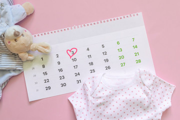 Set of newborn accessories in anticipation of  child - calendar with circled number 3 (three) baby clothes, toys on pink background. Copy space, flat lay, top view.