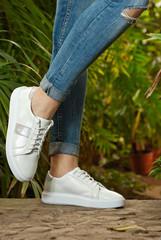 Female legs close-up. Sports sneakers on asphalt against green plants. Shoes in a tropical climate arranger.