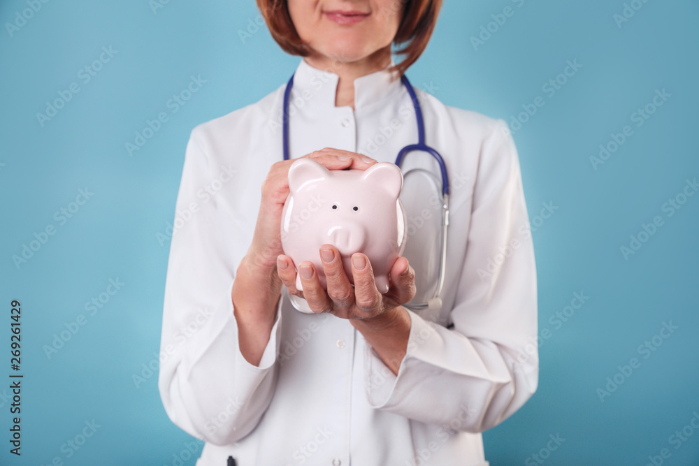 Wall mural medical professional holds piggy bank on blue background