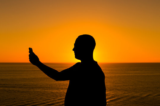 silhouette of a young man using mobile phone at sunset. Ocean background. Vacation and technology concept