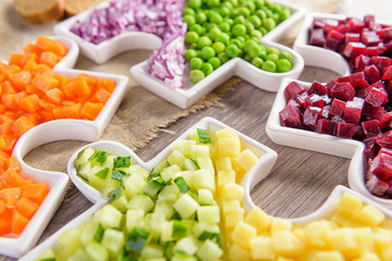 Delicious fresh pieces of vegetables of carrots, cucumber, potatoes, beets and peas close-up with fresh onion and olive oil on a bag cloth on a rustic gray table.