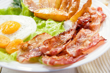 Morning breakfast with delicious fried bacon, French fries and tender egg, close-up.